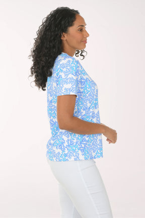 Woman wearing a blue patterned top and white pants on a white background