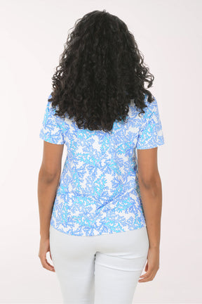 Woman wearing a blue patterned top and white pants on a white background