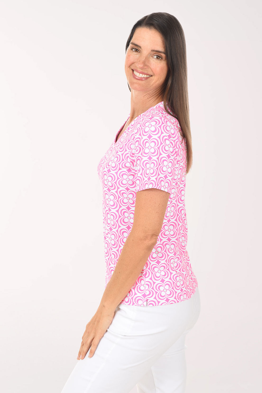 Woman wearing a pink patterned top and white pants on a white background