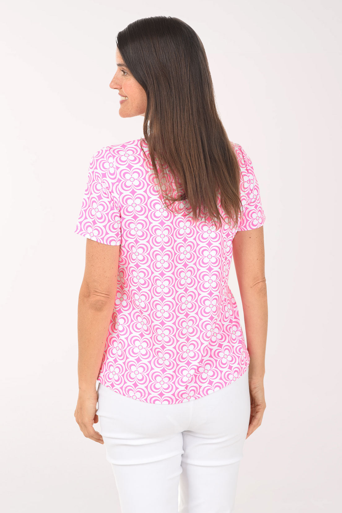 Woman wearing a pink patterned top and white pants on a white background