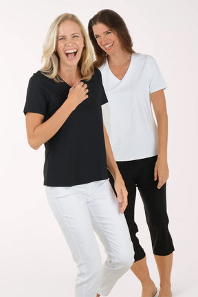 Two women wearing black and white tops with white pants on a white background
