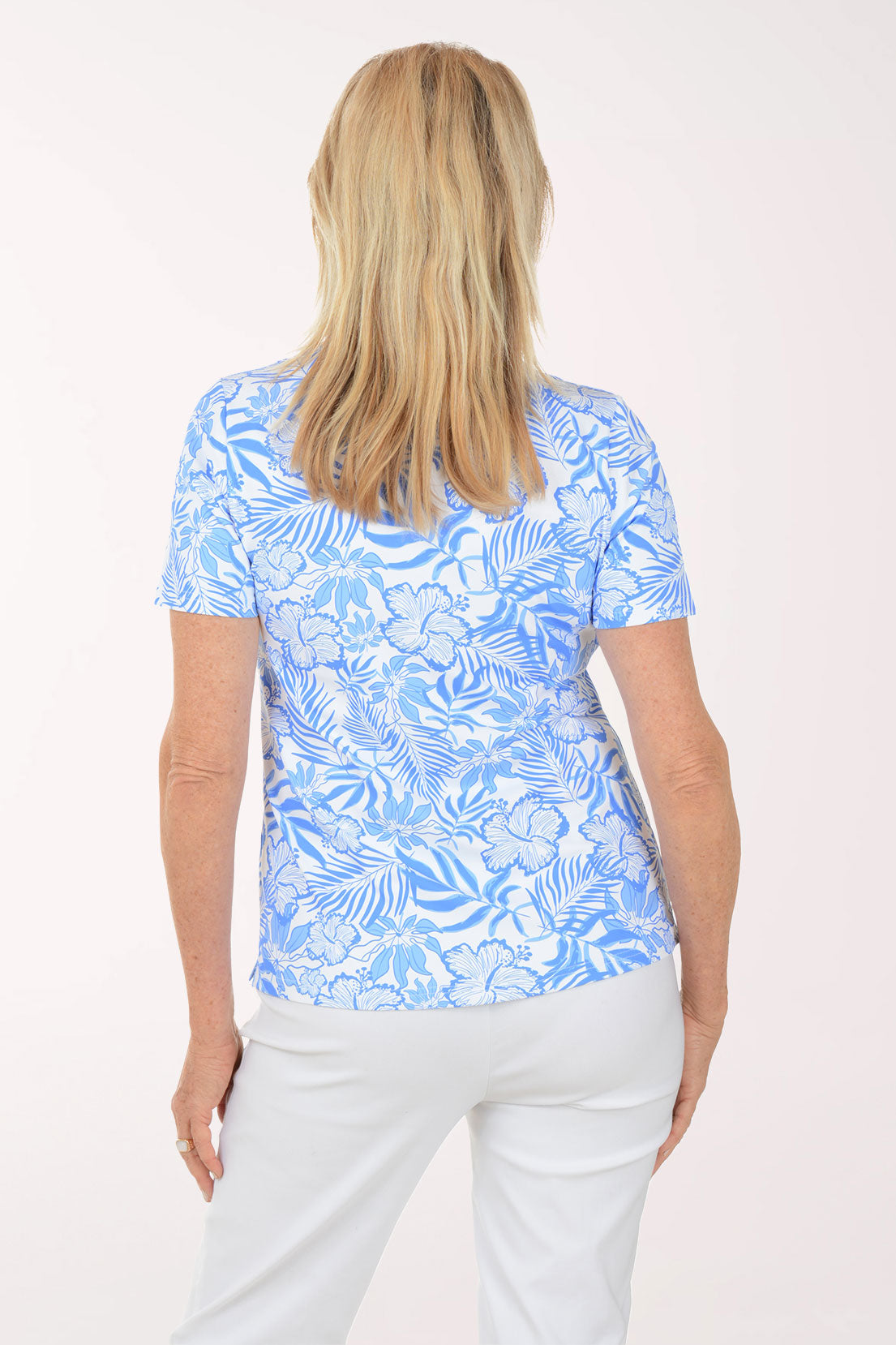 Woman wearing a blue floral patterned shirt and white pants on a white background