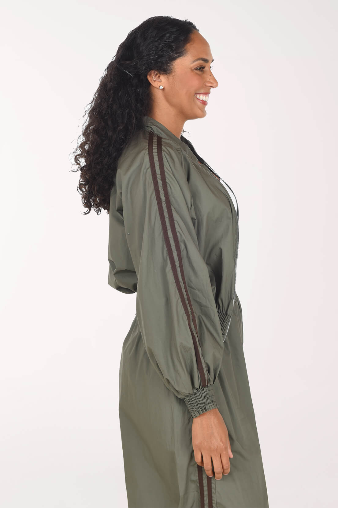 A woman shown in side profile wearing an olive green hooded jacket with dark brown stripes down the sleeves, photographed against a plain white studio background.