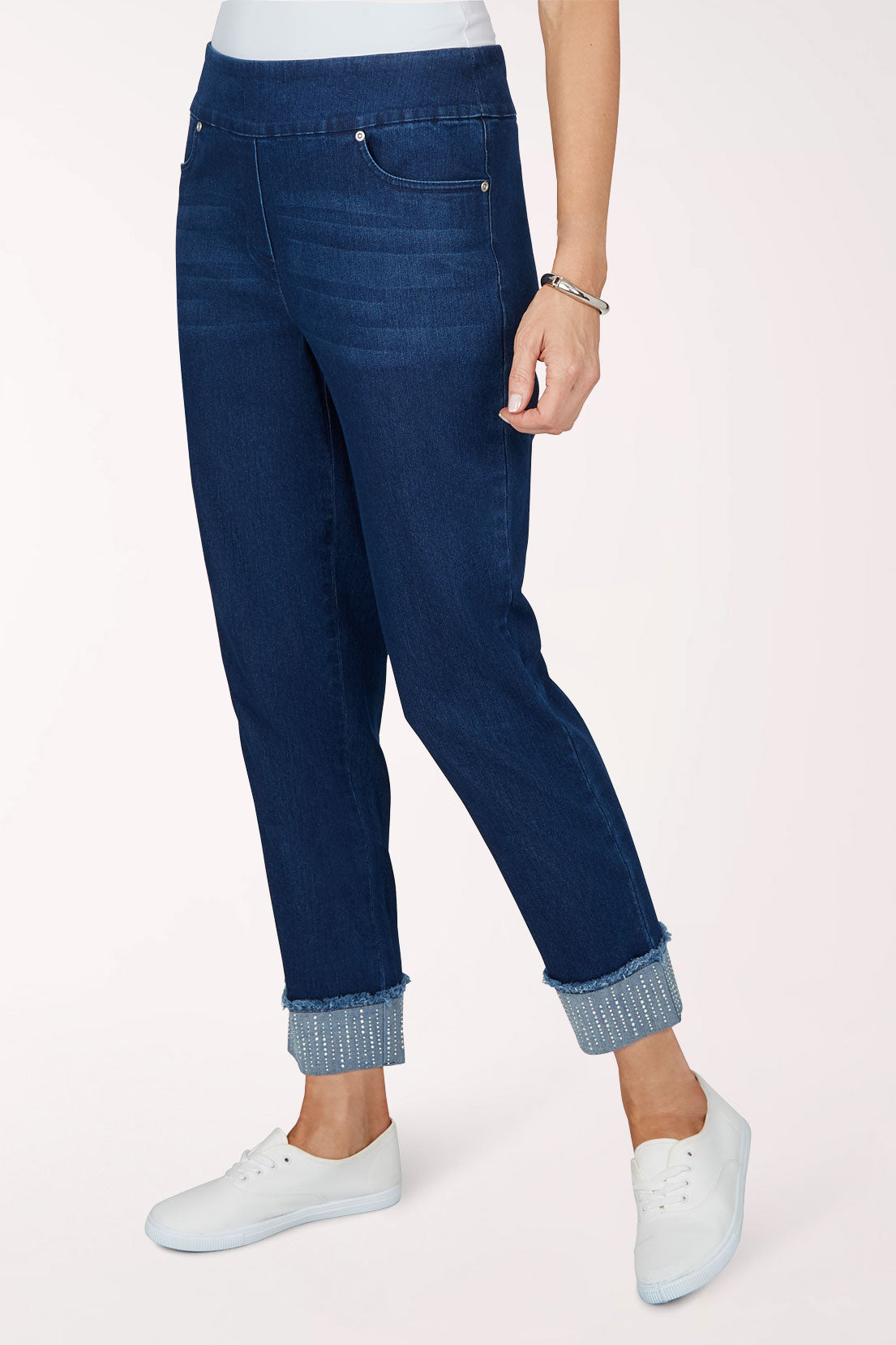 Three-quarter view of the dark indigo pants with one hand in the pocket, showing the rhinestone-trimmed rolled cuffs.