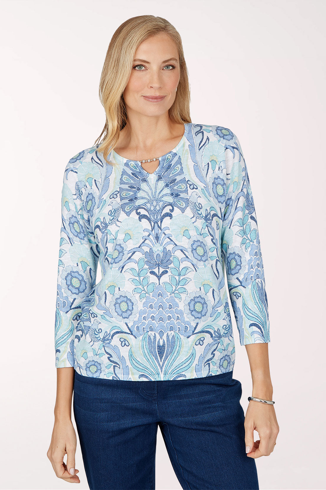 Front view of a woman in a scoop neck sweater with a light blue and white damask print in blue, aqua and navy, a small beaded keyhole at the neckline and 3/4 sleeves, worn with dark jeans.