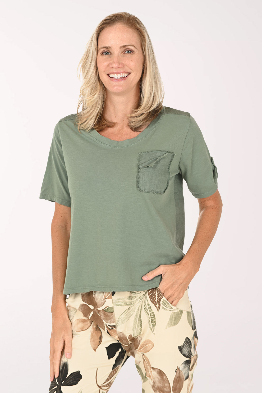 Woman wearing a green t-shirt with a pocket and floral pants on a white background