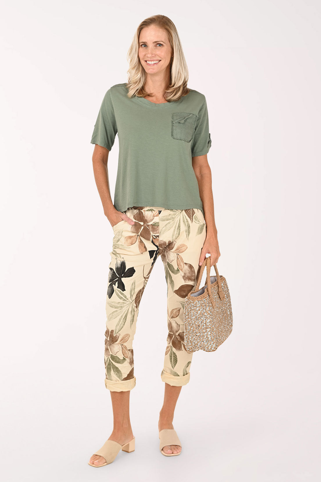 Woman wearing a green top and floral pants, holding a straw bag on a white background