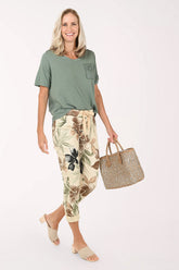 Woman wearing a green top and floral pants, holding a straw bag on a white background