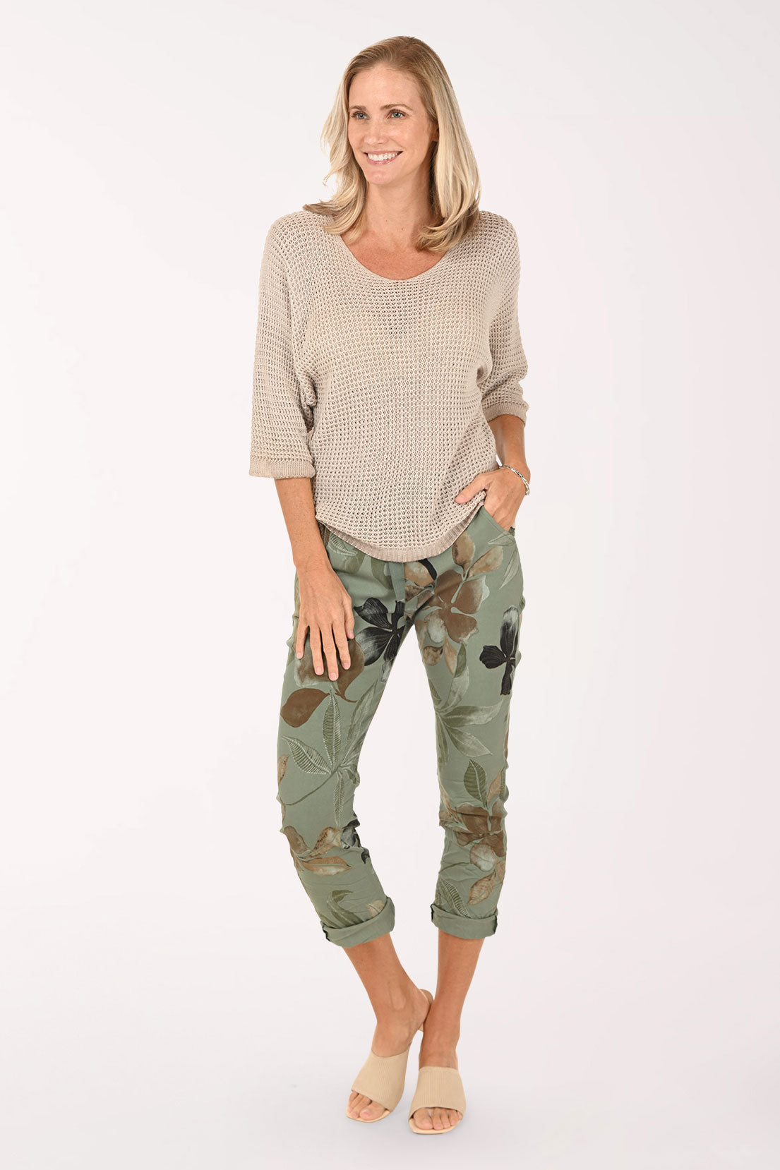 Woman wearing a beige sweater and green floral pants on a white background