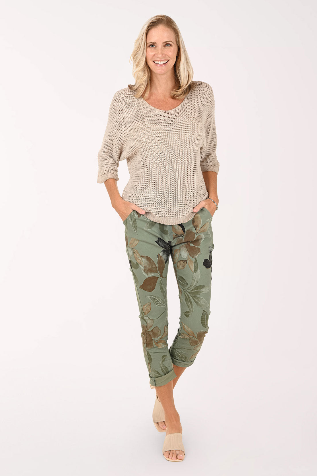 Woman wearing a beige sweater and green floral pants on a white background