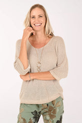 Woman wearing a beige knitted sweater with floral pants on a white background