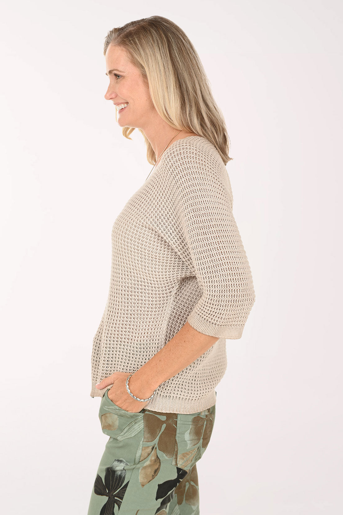 Woman wearing a beige knitted sweater with floral pants on a white background