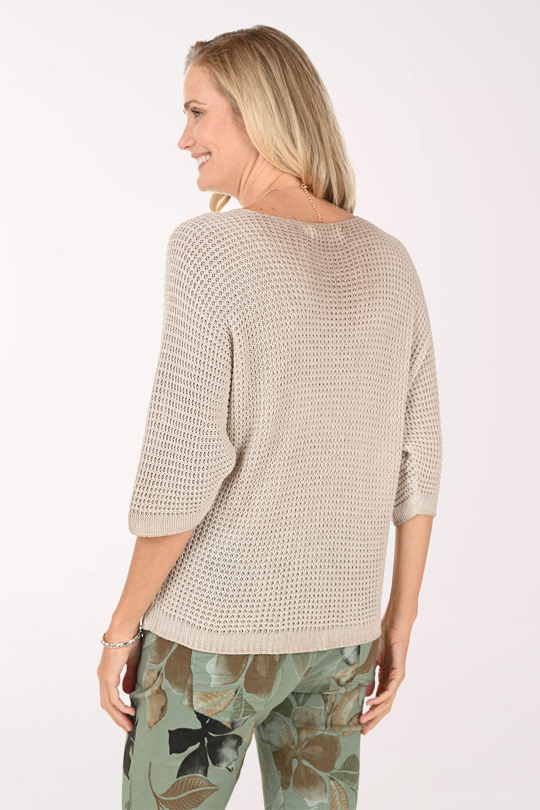 Woman wearing a beige knitted sweater with floral pants on a white background