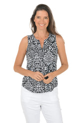 Woman wearing a black and white patterned sleeveless top with white pants on a white background