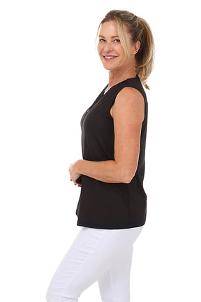 Woman wearing a black sleeveless top and white pants on a white background. Side shot.