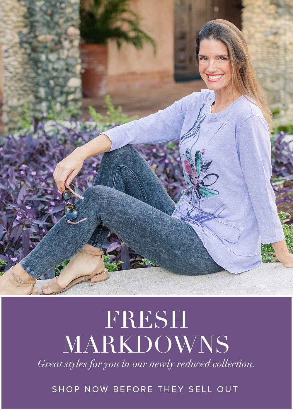 Woman sitting outdoors wearing a light purple sweater with a floral design and black leggings.