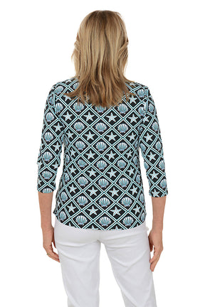 Woman wearing a patterned blouse with white pants on a white background. Back shot.