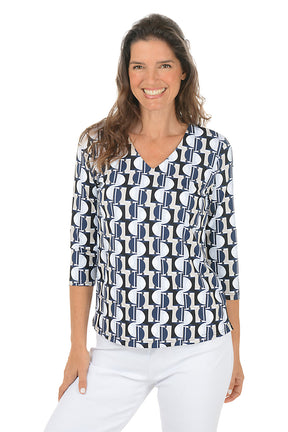 Woman wearing a v-neck 3/4 sleeve half moon geometric patterned blouse in black, tan and blue with a white background.