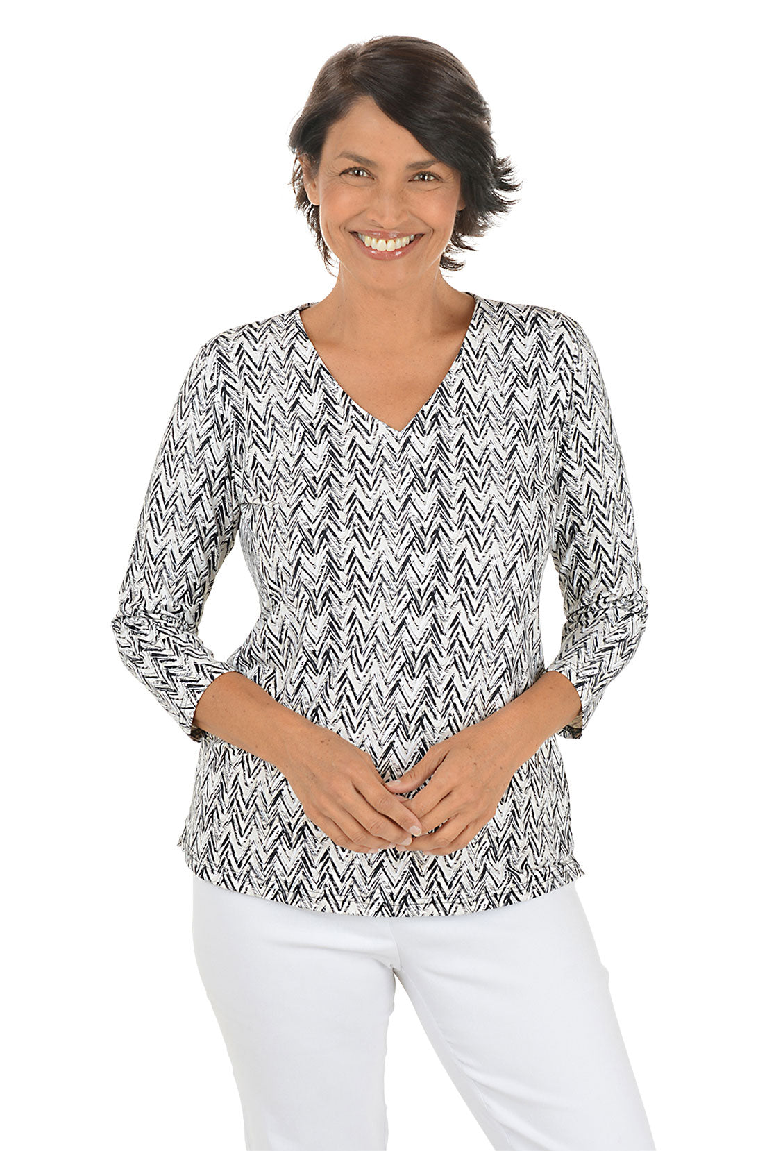 Woman wearing a 3/4 sleeve sandy-colored chevron print patterned top and white pants on a white background.