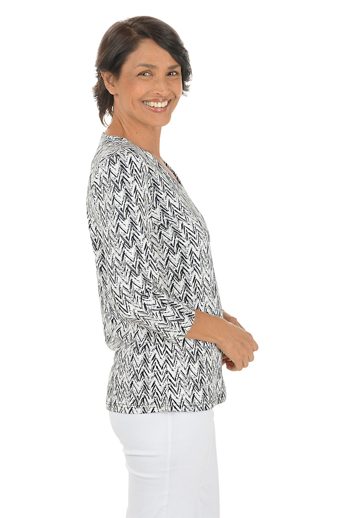 Woman wearing a 3/4 sleeve sandy-colored chevron print patterned top and white pants on a white background. Side shot.