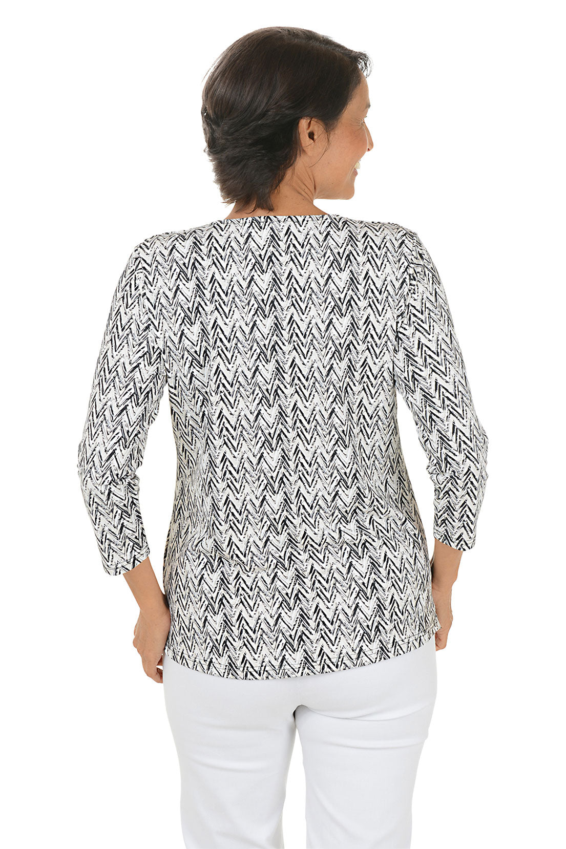 Woman wearing a 3/4 sleeve sandy-colored chevron print patterned top and white pants on a white background. Back shot.