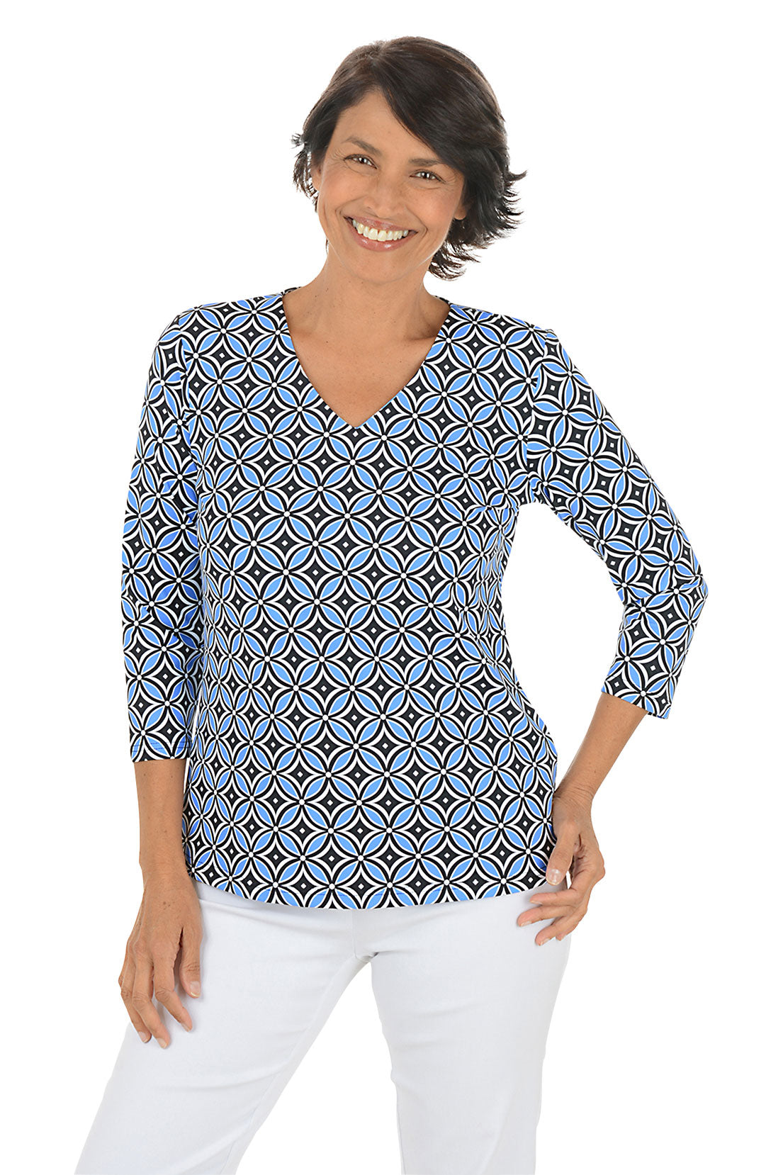 Woman wearing a geometric patterned blue and black blouse with white pants on a white background.
