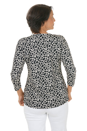 Woman wearing a black and white giraffe patterned blouse with white pants on a white background. Back shot.
