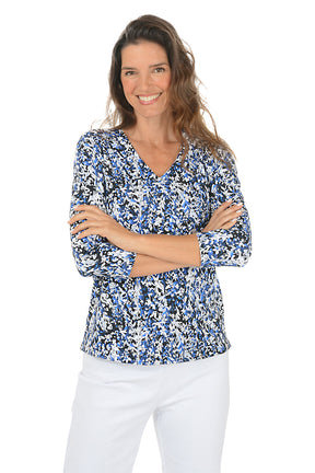 Woman wearing a 3/4 sleeve blue floral blouse and white pants on a white background.