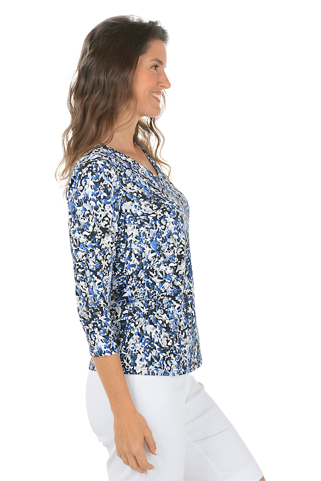 Woman wearing a 3/4 sleeve blue floral blouse and white pants on a white background. Side shot.