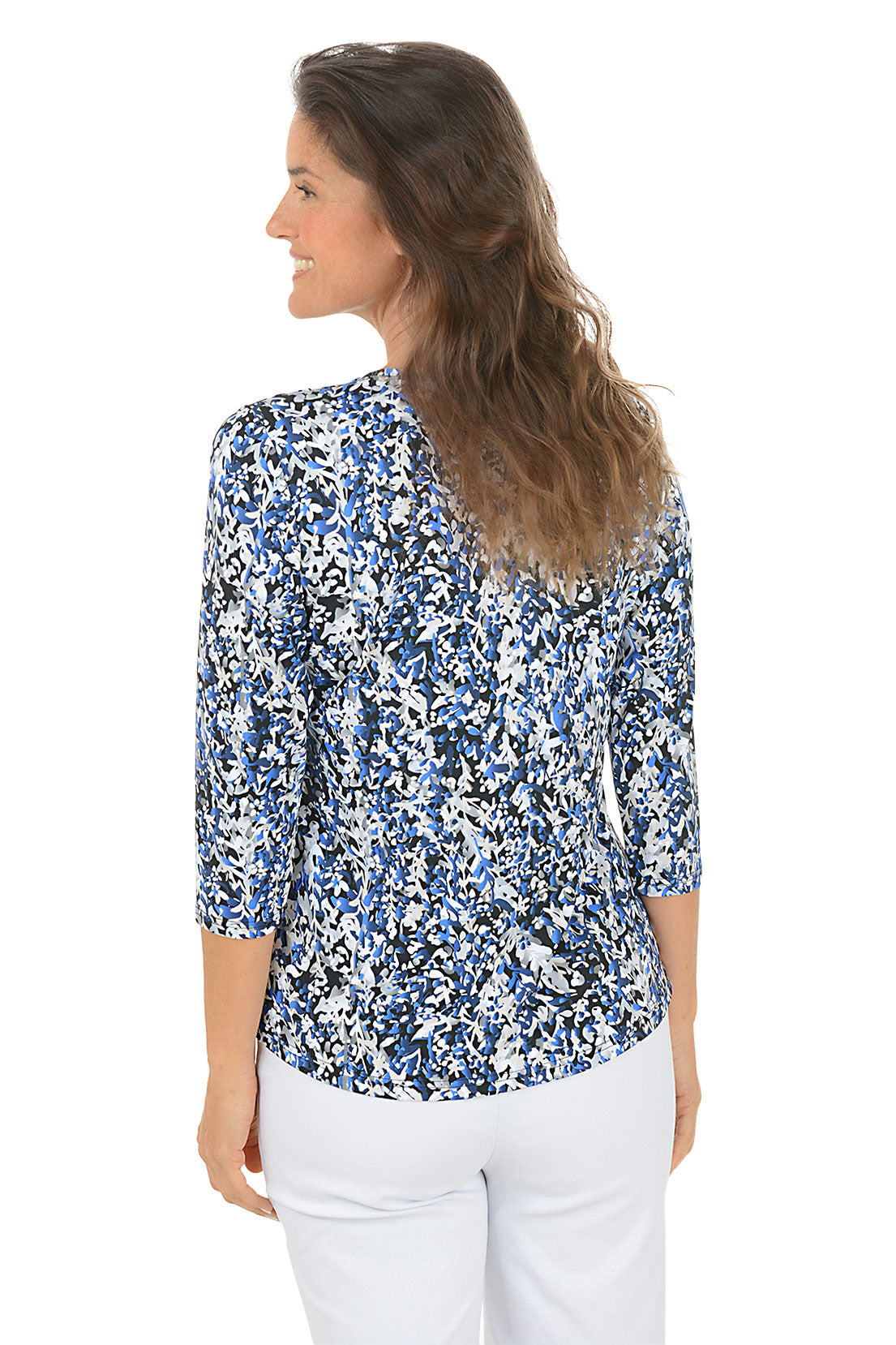 Woman wearing a 3/4 sleeve blue floral blouse and white pants on a white background. Back shot.