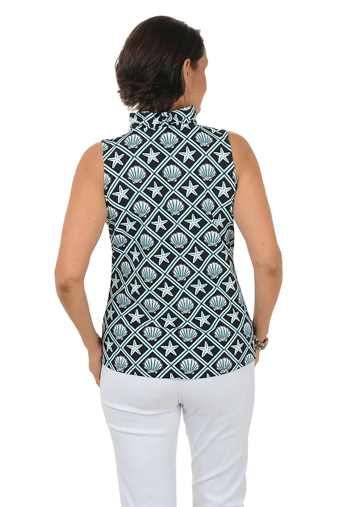 Woman wearing a sleeveless top with shell pattern and white pants on a white background