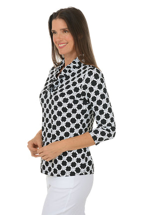 Woman wearing a black and white patterned blouse with white pants on a white background. Side shot.