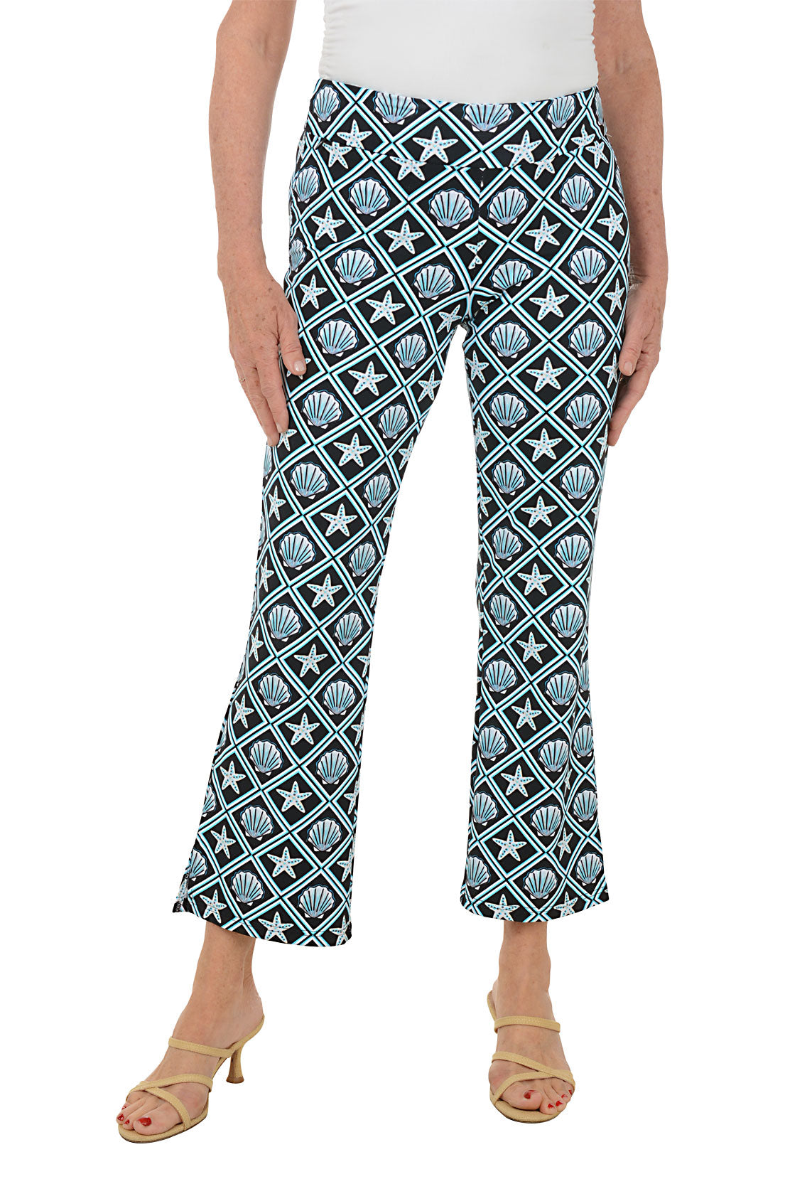 Woman wearing patterned seashell pants with a white top on a white background.