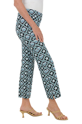 Woman wearing patterned seashell pants with a white top on a white background. Side shot.