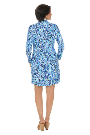 A woman wearing a long sleeve dress with a blue vine pattern and half-zip placket  detail along the neckline. Back shot.
