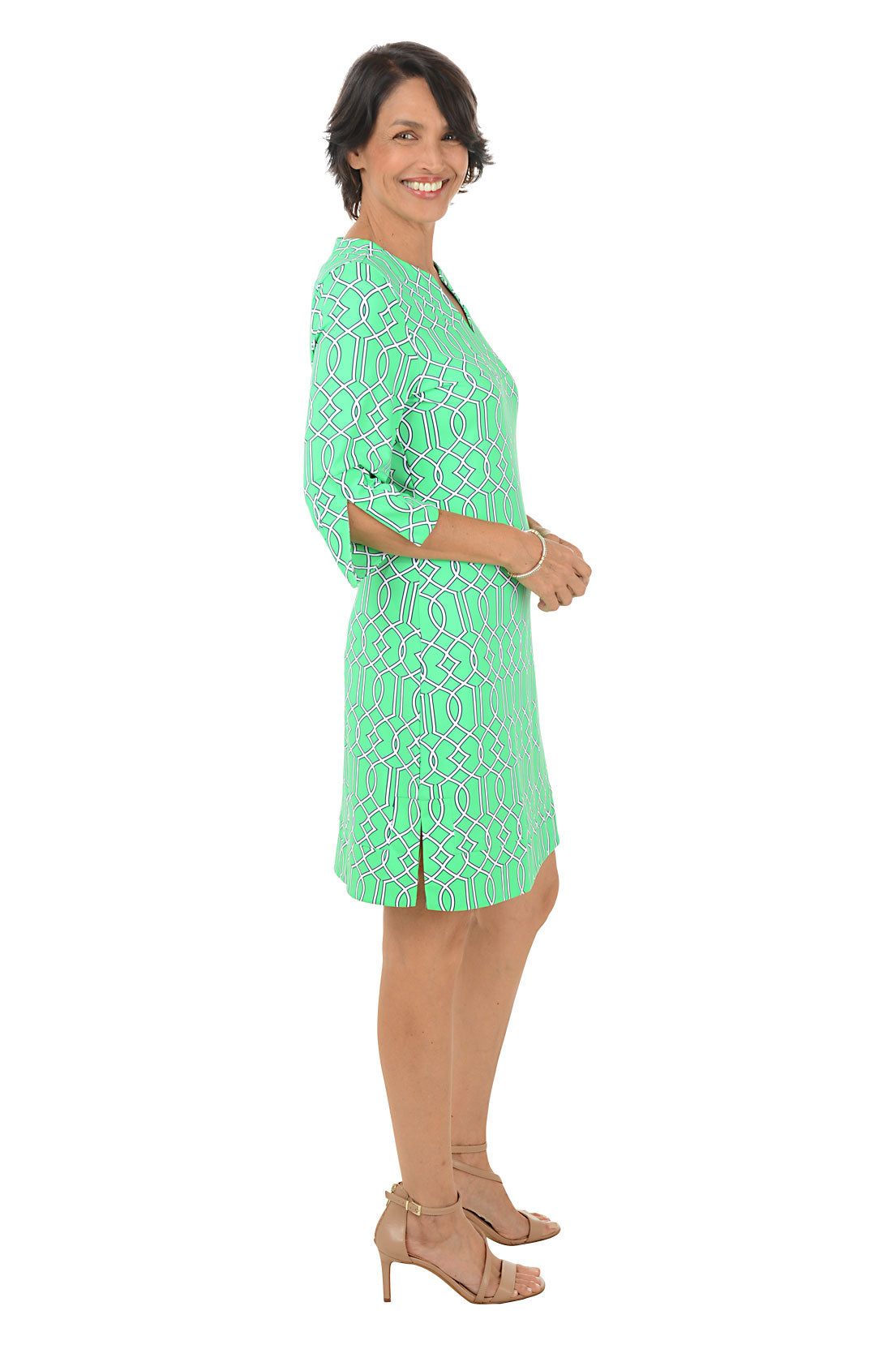 Woman wearing a green patterned dress on a white background. Side shot.