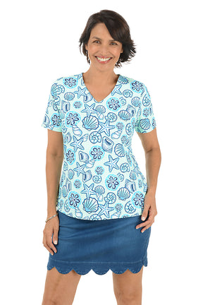 Woman wearing a blue patterned blouse with a shell design and a scallop denim skort on a white background.