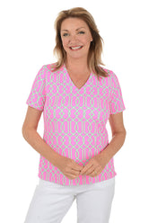 Woman wearing a pink patterned blouse with white pants on a white background.