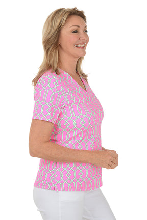 Woman wearing a pink patterned blouse with white pants on a white background. Side shot.