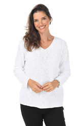 A woman wearing a long sleeve white cotton V-neck sweater and black pants.