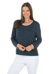 A woman wearing a scoop neck navy sweater with contrast white piping.