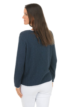 A woman wearing a scoop neck navy sweater with contrast white piping. Back shot.