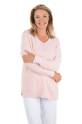 Woman wearing a light pink sweater and white pants on a white background