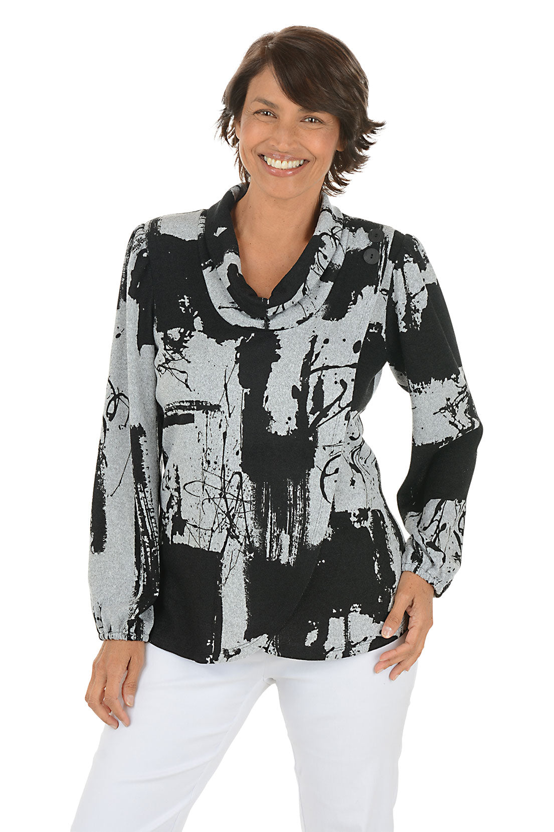 Woman wearing a black and white abstract patterned blouse with white pants on a white background.