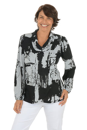 Woman wearing a black and white abstract patterned blouse with white pants on a white background.