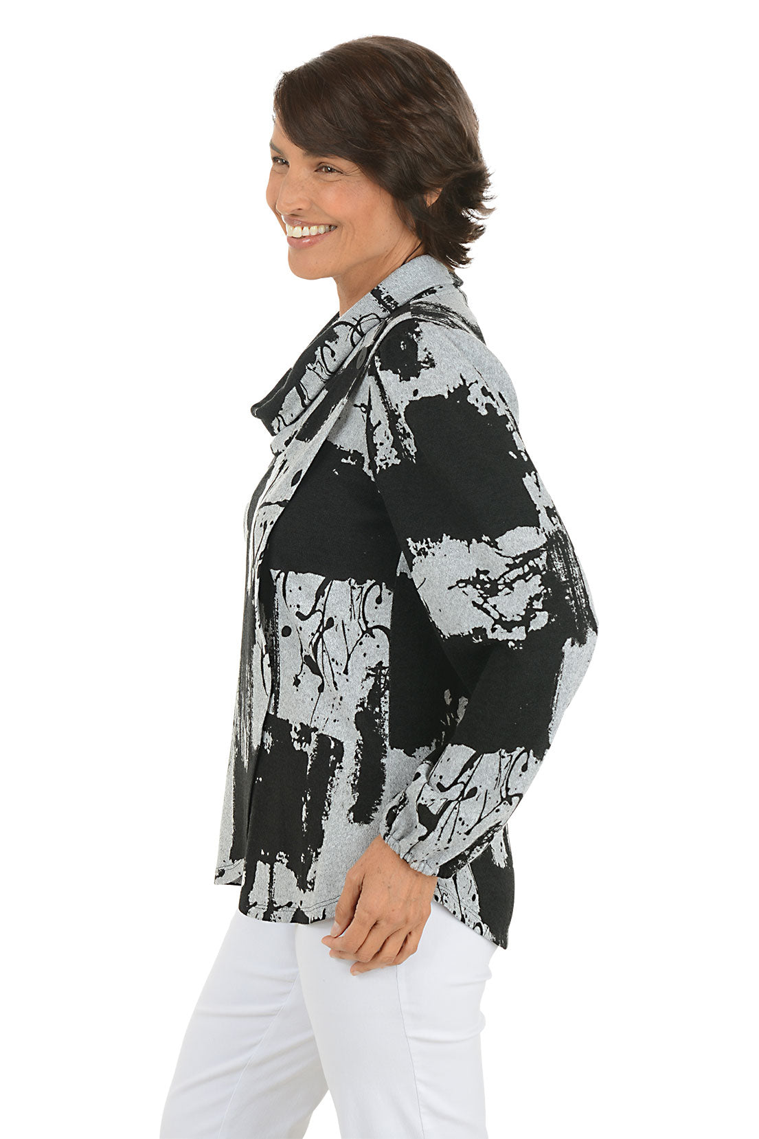 Woman wearing a black and white abstract patterned blouse with white pants on a white background. Side shot.