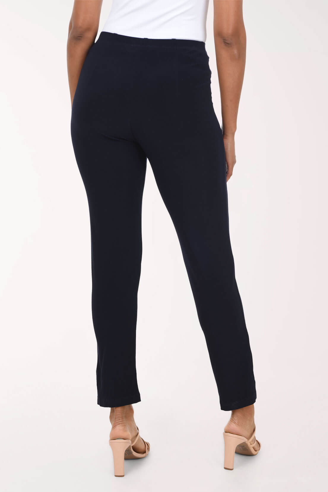 A person shown from the back wearing slim navy cropped pants with a white top and beige heeled sandals against a plain light background.