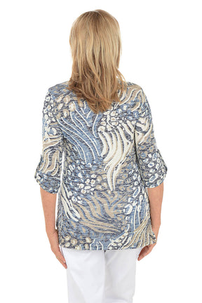 Woman wearing a patterned blouse with white pants on a white background. Back shot.