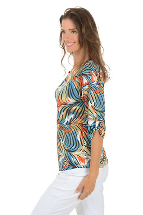 Woman wearing a colorful patterned top and white pants on a white background. Side shot.