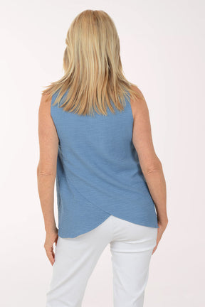 Woman wearing a blue sleeveless top and white pants on a white background